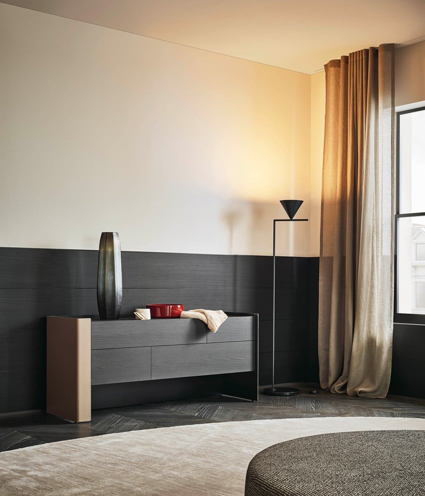 Chloe chest of drawers with external structure in hide 29 tortora and internal structure in glossy brown nickel, drawers and top in black elm. New York pouf with removable cover in fabric Zante 10 nero and feet in glossy brown nickel. Carpet Frame perla.