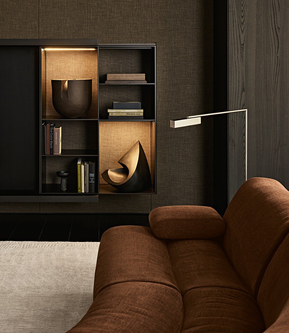 Ernest sofa in removable fabric Yukon 27 tabacco. Surface wall panelling in fabric Mesh bronzo, black elm and glossy lacquer tundra, mat ardesia profiles. Wall mounted Code composition, open storage units in mat lacquer bronzo with backs in fabric Mesh bronzo and integrated led light. Storage units with Tape slatted doors in black elm and transparent glass, mat ardesia frame and handle, inner structure in black elm with backs in fabric Mesh bronzo and integrated led light. Carpet Trace white.