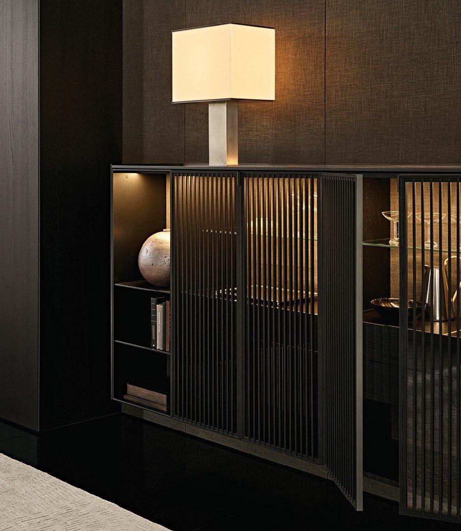 Surface wall panelling in fabric Mesh bronzo, black elm and glossy lacquer tundra, mat ardesia profiles. Wall mounted Code composition, open storage units in mat lacquer bronzo with backs in fabric Mesh bronzo and integrated led light. Storage units with Tape slatted doors in black elm and transparent glass, mat ardesia frame and handle, inner structure in black elm with backs in fabric Mesh bronzo and integrated led light. Carpet Trace white.