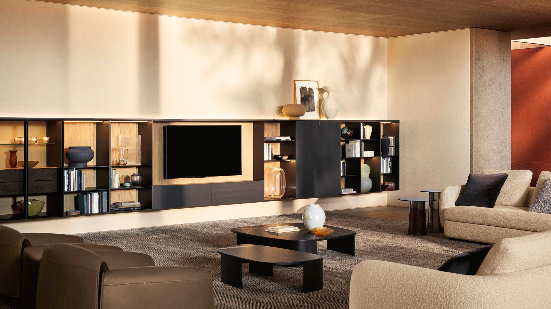 Composition of wall-mounted Code storage units. Doors with bronze metal lacquer finish. Handle with matt slate finish; in reflective transparent glass, frame and handle with matt slate finish. Backlit top and side panels with bronze metal lacquer finish. Open compartments and structure with bronze matt lacquer finish. Walls of open compartments and TV stand in Gold oak, walls of storage units with shelves covered in light linen textile. TV stand with storage units with drop-down doors. Front with bronze metal lacquer finish. Display units with internal transparent glass shelves and drawers with bronze metal lacquer finish. Top in polished Zecevo marble. Integrated LED lighting. Saint-Germain sofa in white Siro fabric (01) with removable covers, cushions in chocolate Brest fabric (11), burnt ochre Persia velvet (2020) and cream Glasgow velvet (01). Legs with Brown Nickel matt nickel finish. Le Club armchairs with Silk leather finish in roccia (06), non-removable cover. Koishi coffee tables with polished Sahara Noir marble top; polyester finish. Structure in painted black steel. Orbit coffee tables, top and structure in bronze glass, blown glass structure. Cannelè carpet.
