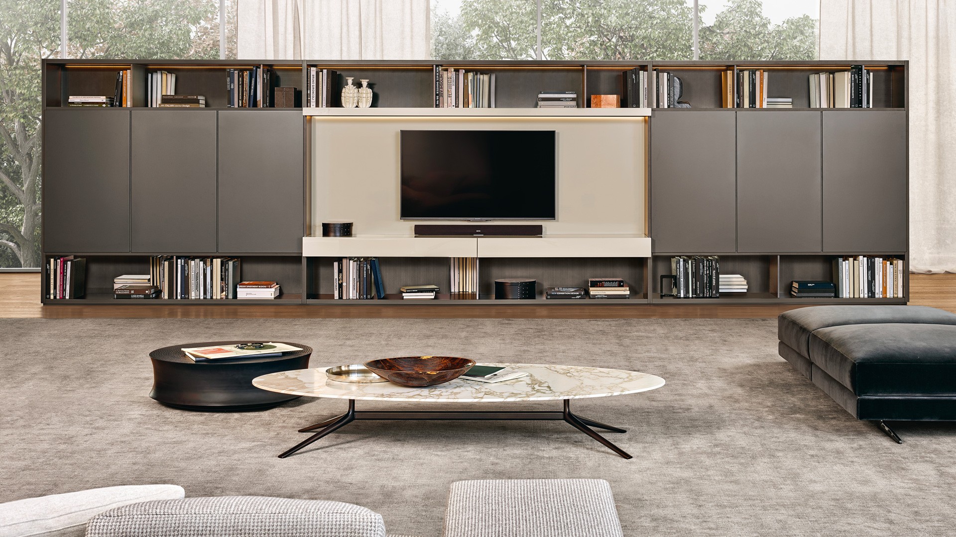 Система корпусных модулей Wall System: структура и распашные двери Slim с лакированной матовой отделкой цвета визоне. Стенки и боковые панели с лакированной металлической отделкой титанового цвета. Стойка для телеаппаратуры с лакированной матовой отделкой цвета канапа и откидной дверью Jet. Встроенная светодиодная подсветка. Журнальный столик Mondrian с овальной столешницей из матового мрамора Calacatta Oro и структурой с никелированной глянцевой отделкой Brown Nickel. Журнальный столик Soori из металла с отделкой под антикварную бронзу. Пуф Mondrian, съемный чехол из бархата Persia цвета карбоне (1404). Ножки с никелированной глянцевой отделкой Brown Nickel.