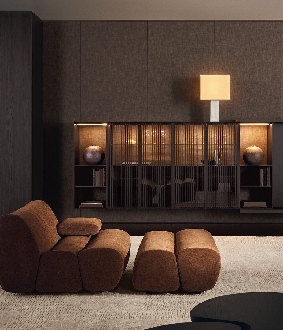 Ernest chaise longue in removable fabric Yukon 27 tabacco. Wall mounted Code composition, open storage units in mat lacquer bronzo with backs in fabric Mesh bronzo and integrated led light. Storage units with Tape slatted doors in black elm and transparent glass, mat ardesia frame and handle, inner structure in black elm with backs in fabric Mesh bronzo and integrated led light. Backlit top and sides in metal lacquer bronzo. Carpet Trace white.