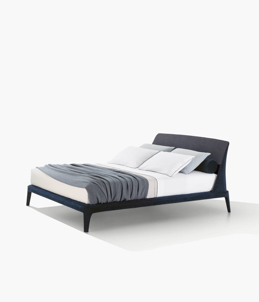 Kelly bed, padded headboard and bed frame with removable covering in fabric Naxos 27 prussia, inner headboard in fabric Kitami 11 oceano. Roll cushions in removable fabric Naxos 27 prussia. Coordinated bed linen in cotton Provence 01 bianco with profile in nero and 08 polvere with profile in polvere. Blanket Linus grafite.
