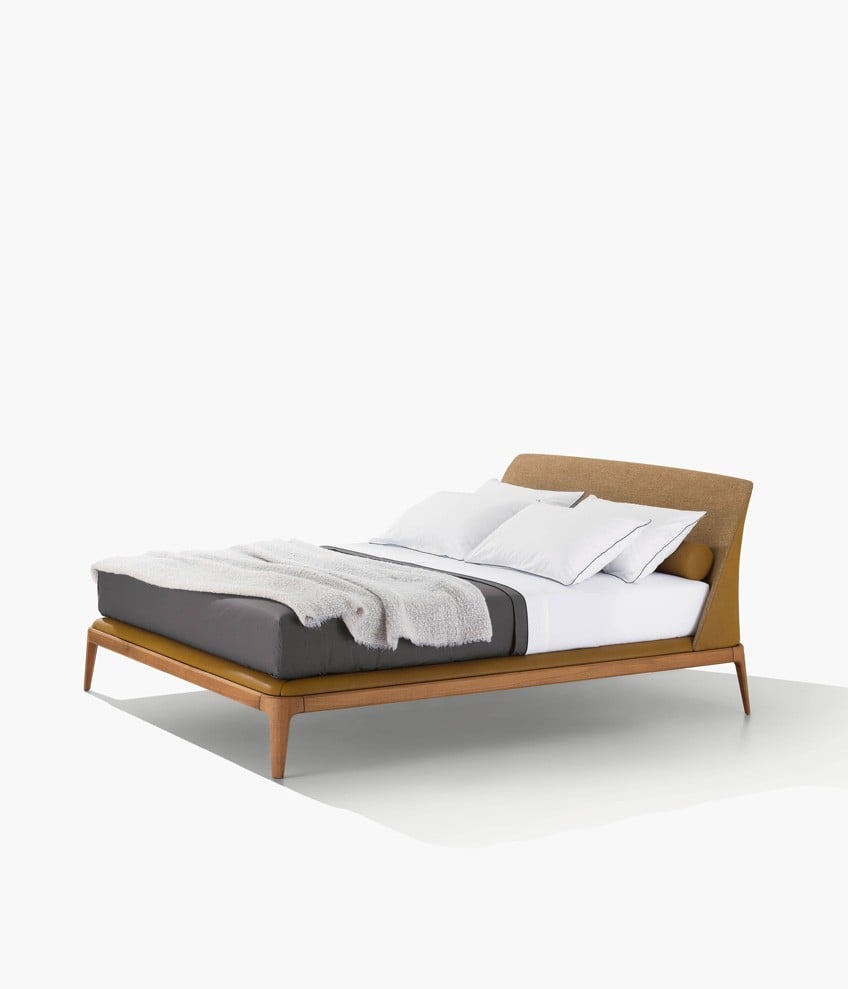 Kelly bed, padded headboard with non-removable covering, outer headboard and roll cushions in leather Silk 12 senape, inner headboard in fabric Arcadia 05 bronzo. Bed frame in gold walnut and inner part with non-removable covering in leather Silk 12 senape. Matching bed linen in cotton Provence 01 bianco and 07 grafite with profiles in nero.