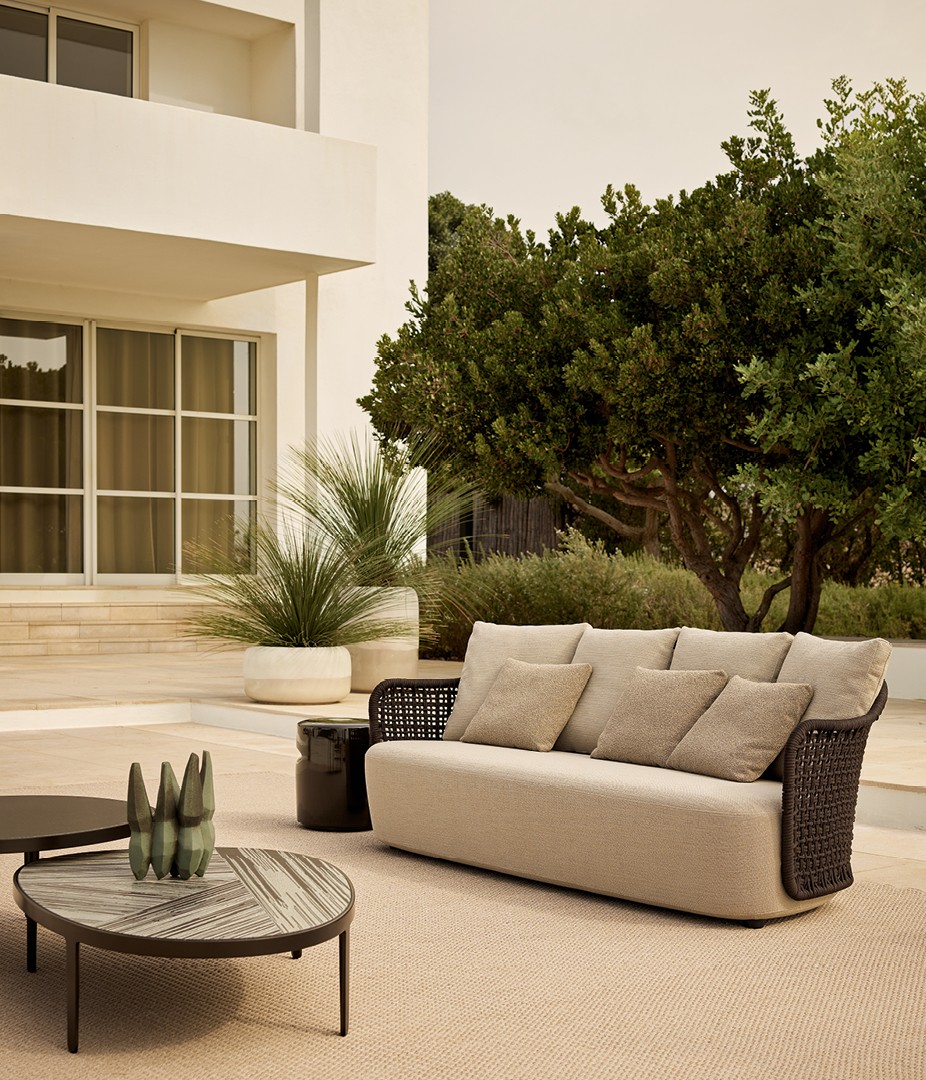 Диван Mad Out со структурой из нержавеющей стали, покрытой веревкой testa di moro, спинка из плетеной веревки testa di moro. Съемный чехол из ткани Karif 03 sabbia, подушки из ткани Nashi 04 sabbia. Журнальные столики Mad Out со структурой из матового коричневого никеля, столешницы из лавового камня nera, также с декором из литого стекла. Журнальный столик Azu из глянцевого глазурованного керамогранита bronzo. Ковер Kamir corda. Вазы Crew из матового глазурованного керамогранита sabbia с глянцевой глазурованной нижней частью.