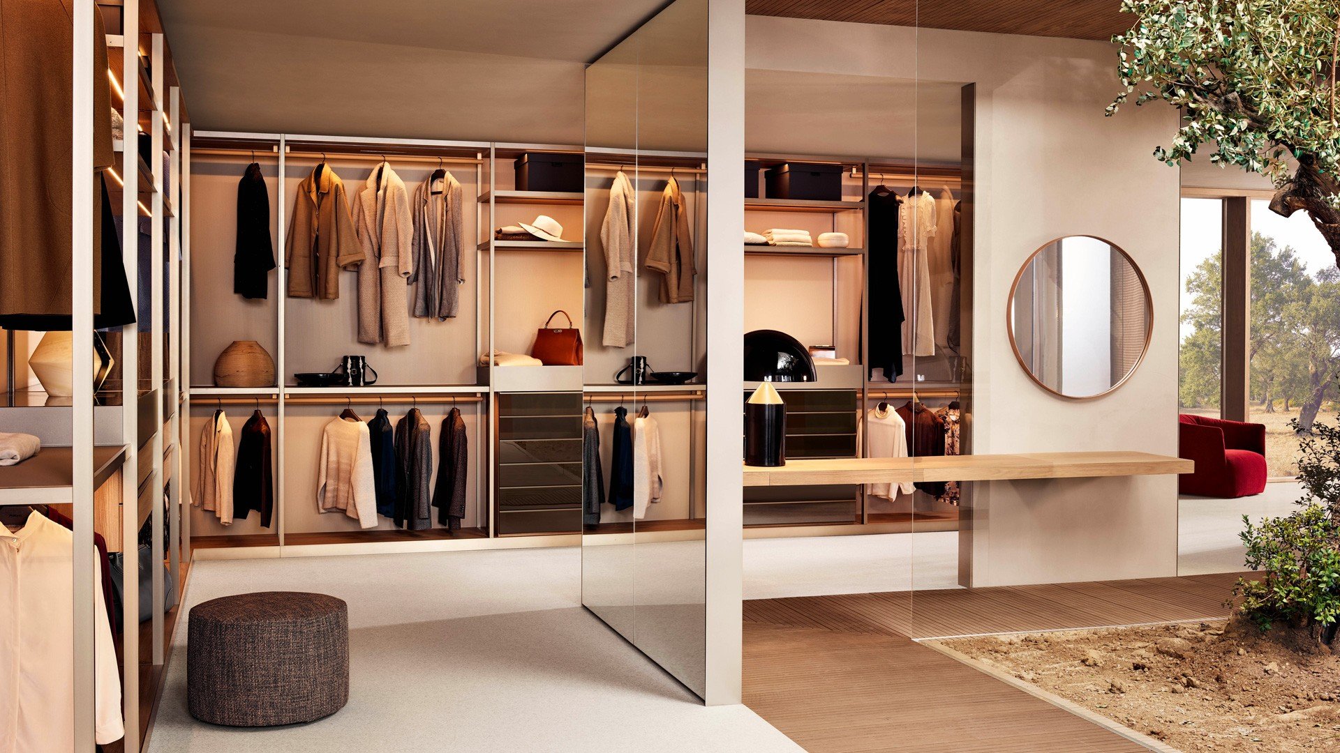 Cabina armadio Senzafine con struttura in nobilitato olmo, fianchi a telaio, bordi e fascia zoccolo in champagne opaco, schienali in metacrilato roller latte. Ripiani superiori in nobilitato olmo e frontale champagne opaco, luce led integrata. Tubi appendiabiti rivestiti in tecnoover 06 nocciola e champagne opaco. Ripiani inferiori in tecnocover 06 nocciola con telaio champagne opaco. Cassettiere a vetrina con piano superiore in vetro fumé, cassetto con frontale a smusso in laccato opaco champagne e piano in tecnocover 06 nocciola. Cassetti inferiori in nobilitato olmo e in vetro riflettente fumé con maniglia Track champagne opaco. Pouf New York in tessuto sfoderabile Antea 05 terra di siena. Specchio Circle con cornice in cuoio 26 invecchiato e specchio bianco. Poltrona Santa Monica in velluto sfoderabile Tebe 11 bruciato.
