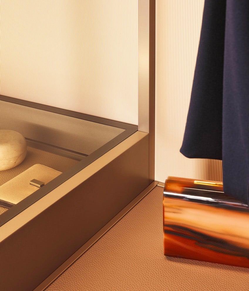 Close up of the display case chest of drawers with top in fumé glass, shelf in techno leather 06 nocciola and integrated led light, next to it, shelf in techno cover 06 nocciola with mat champagne frame.