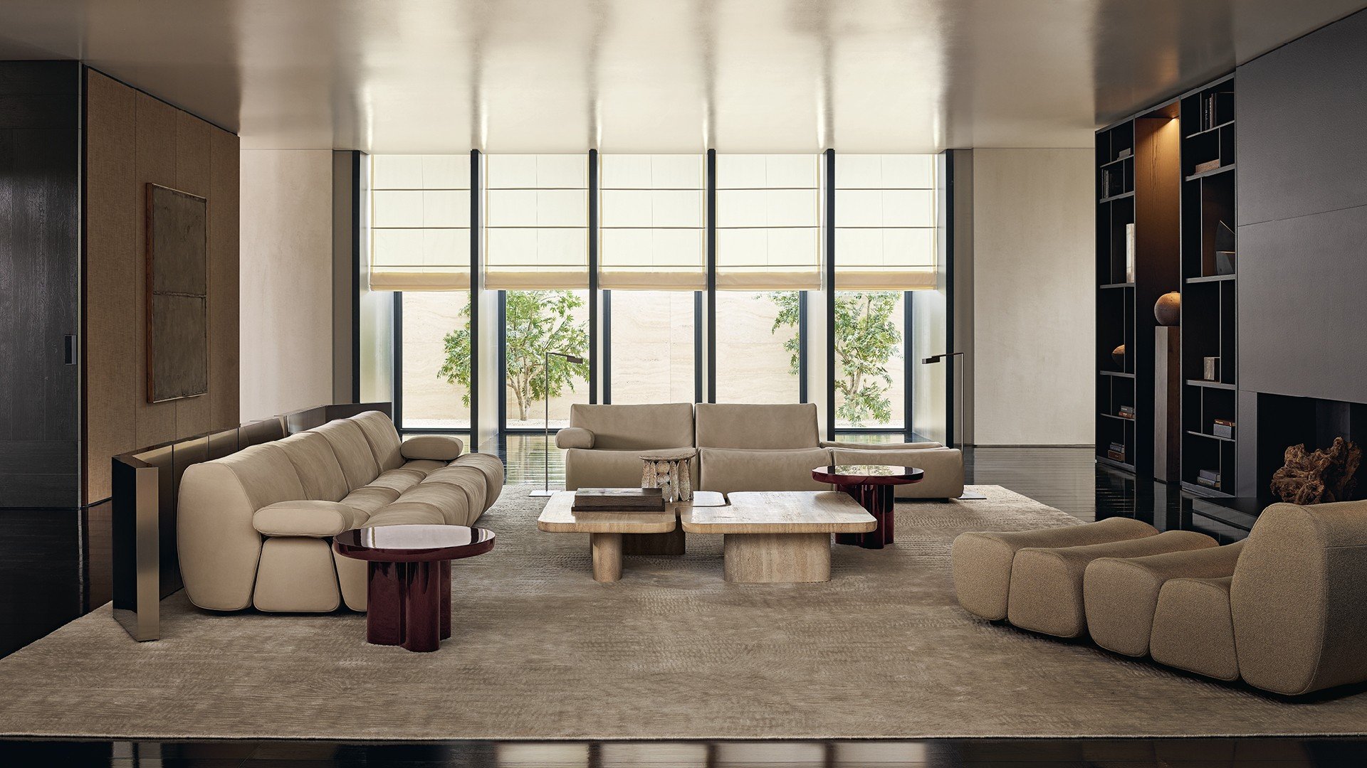 Ernest sofas in removable leather Nabuk 01 latte, chaise longue in removable fabric Altair 02 corda. Ernest coffee tables in mat marble travertino classico and in glossy lacquer mosto. Surface wall panelling in fabric Mesh bronzo with mat ardesia profiles. Wall System composition with structure and recessed shelves in black elm, grids and backs in metal lacquer bronzo, compartments with Stage backs in fabric Mesh moka, integrated led light. Carpet Trace white.