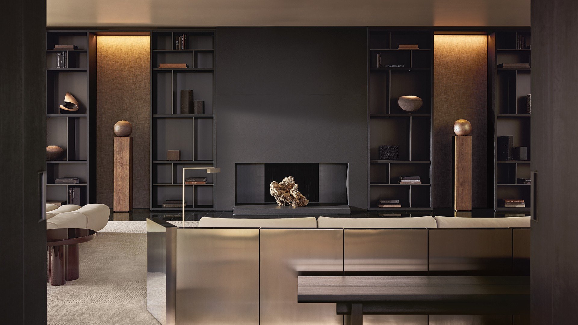 Surface wall panelling in fabric Mesh bronzo with mat ardesia profiles. Wall System composition with structure and recessed shelves in black elm, grids and backs in metal lacquer bronzo, compartments with Stage backs in fabric Mesh moka, integrated led light. Carpet Trace white.