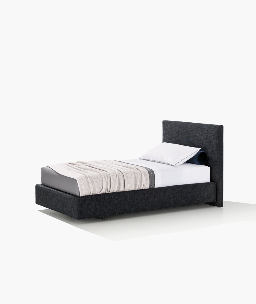 Arca single bed, padded headboard and bed frame with removable covering in fabric Caleo 11 navy. Roll cushions in fabric Persia 54 prussia. Matching bed linen in cotton Provence 01 bianco with profile in roccia and 06 roccia with profile in bianco. Linus blanket latte.