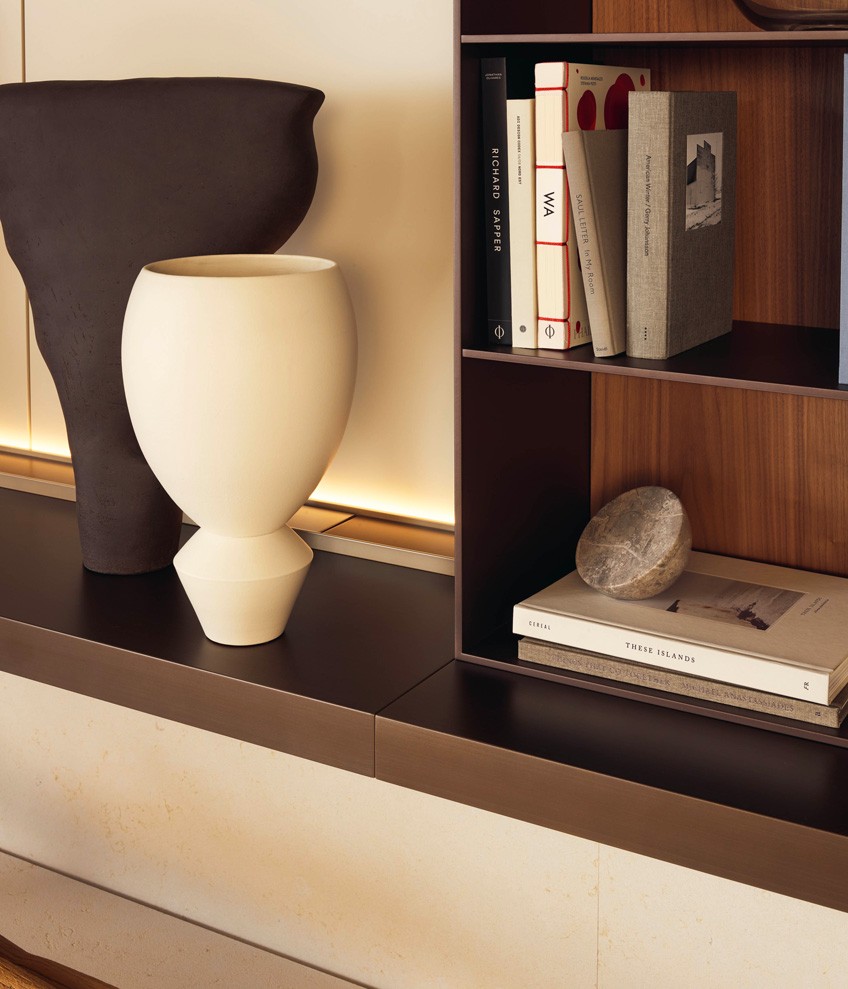 Система навесных корпусных модулей Code с полкой с подсветкой с лакированной металлической отделкой цвета латуни. Канал с кабельными вводами с матовой отделкой цвета шампанское. Декоративные панели с лакированной матовой отделкой цвета канапа и профилями с матовой отделкой цвета шампанское. Книжный шкаф с лакированной матовой отделкой цвета латуни со стенками из ореха Gold. Кресла Gentleman Relax и пуф Gentleman, съемные чехлы из ткани Siro цвета лино (02). Диван Gentleman’s Friends, съемные чехлы из бархата Tebe цвета нотте (08). Основание с никелированной глянцевой отделкой Brown Nickel. Журнальный столик Soori из металла с отделкой под античную бронзу. Ковер Plain цвета тортора.