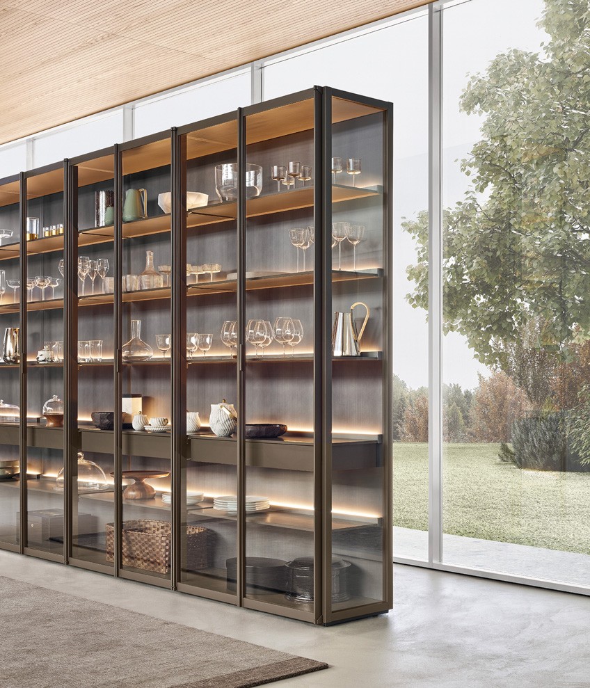 Система корпусных модулей Wall System со структурой, боковыми стенками и рамой Ego Day, полками и навесными ящиками Ego Day с лакированной матовой отделкой цвета визоне. Стенки с лакированной металлической отделкой титанового цвета. Встроенная светодиодная подсветка. Двери и боковые стенки Ego Day из прозрачного стекла и рама с лакированной матовой отделкой цвета визоне. Ковер Plain цвета тортора.