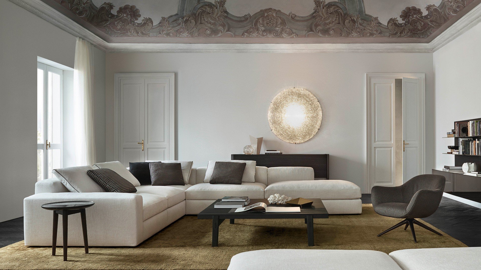 Sofa and pouf Dune with removable cover in fabric Rabat 400 ecru, cushions in fabric Nancy 101 carbone, velvet Persia 1404 carbone and fabric Rabat 400 ecru with border in grosgrain nero. Mad Chair armchair with removable cover in fabric Nancy 101 carbone, mat brown nickel swivel base. Carpet Frame gold.
