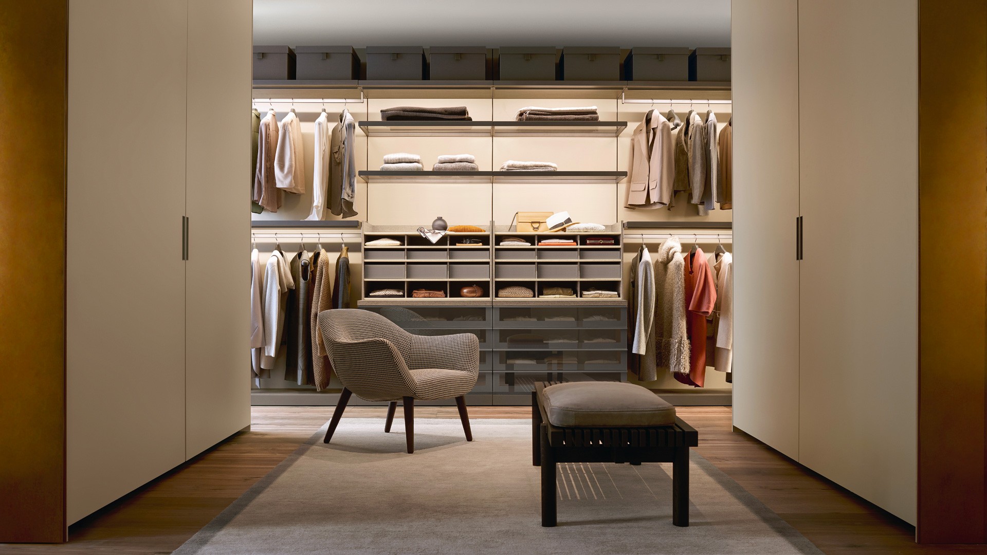 Гардеробная Ubik с настенными панелями из облагороженной плиты Skin с лакированным матовым покрытием цвета латте (94), основаниями из облагороженной плиты из пепельного дуба. Нижний профиль с матовой отделкой цвета ардезия. Полки из облагороженной плиты из пепельного дуба и дымчатого стекла. Рама с лакированной матовой отделкой цвета ардезия. Ящики с фронтальными панелями из облагороженной плиты из пепельного дуба, фасады ящиков из дымчатого отражающего стекла с кромкой и ручками Track с лакированной матовой отделкой цвета ардезия. Сверху устанавливаются корпусные модули для рубашек из облагороженной плиты из пепельного дуба. Полки с покрытием Tecnocover цвета латте (05) и ящики, обтянутые тканью цвета ардезия. Гардеробы Senzafine Skin с компланарными раздвижными дверями из облагороженной плиты Skin с лакированным матовым покрытием цвета латте (94).