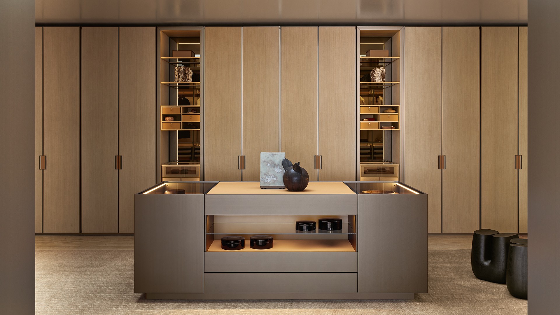 Гардеробная Senzafine из облагороженной плиты ореха blond с боковыми стенками рамы с матовой отделкой цвета champagne; задние части из ткани Mesh écru; боковые части с лакированной металлической отделкой цвета basalto. Оборудование Senzafine Suite, полки из облагороженной плиты ореха blond, сверхпрозрачное стекло с рамой с матовой отделкой цвета champagne, встроенная светодиодная подсветка. Штанги для вешалок с покрытием Tecnocover Grain 10 miele и матовой отделкой цвета champagne. Подставки из облагороженной плиты ореха blond с дном с покрытием Tecnocover Grain 10 miele и перегородкой из облагороженной плиты ореха blond, корзины с покрытием Tecnocover Grain 10 miele и рама из облагороженной плиты ореха blond. Шкаф Senzafine Swing с распашными дверями из прозрачного светоотражающего стекла и рамой с матовой отделкой цвета champagne, ручка Swing (может быть дополнена замком) с покрытием Tecnocover Grain 10 miele и с матовой отделкой цвета champagne; внутренняя часть из облагороженной плиты ореха blond, боковая часть рамы с матовой отделкой цвета champagne, оборудование Senzafine Suite. Остров в виде комода Set Up с лакированной металлической отделкой цвета basalto, верхняя столешница из дымчатого стекла и с покрытием Tecnocover Grain 10 miele, ящики и подставки с ручками с покрытием Tecnocover Grain 10 miele и матовой отделкой цвета basalto, дно с покрытием Tecnocover Grain 10 miele; открытые отделения с полкой из дымчатого стекла. Высокие табуреты Ube из окрашенного массива черного вяза. Ковер Shindo natural.