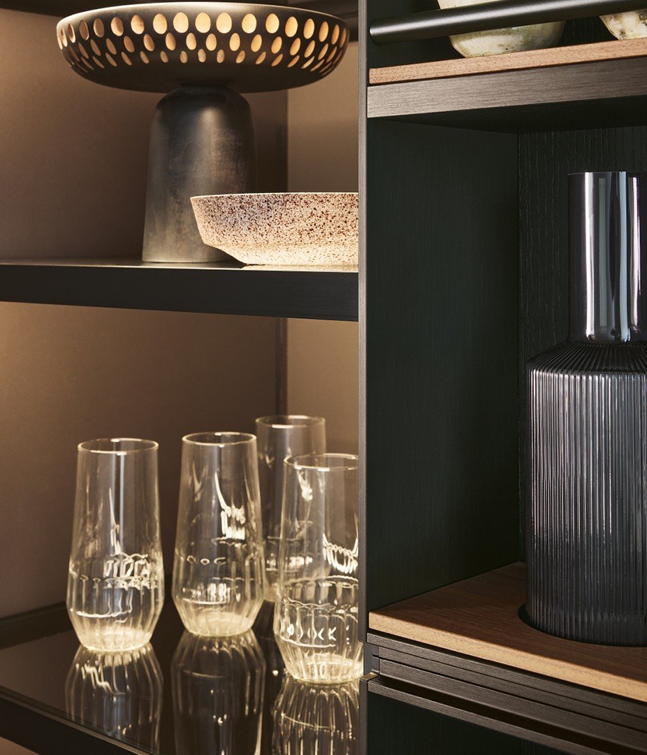 Крупный план системы Deep Shaker Wall с анодированной структурой мока, полками из ореха canaletto и перекладинами в рельефном лаке мока. Высокий пенал с внутренними полками из дымчатого стекла и черной анодированной рамкой, встроенная светодиодная подсветка.