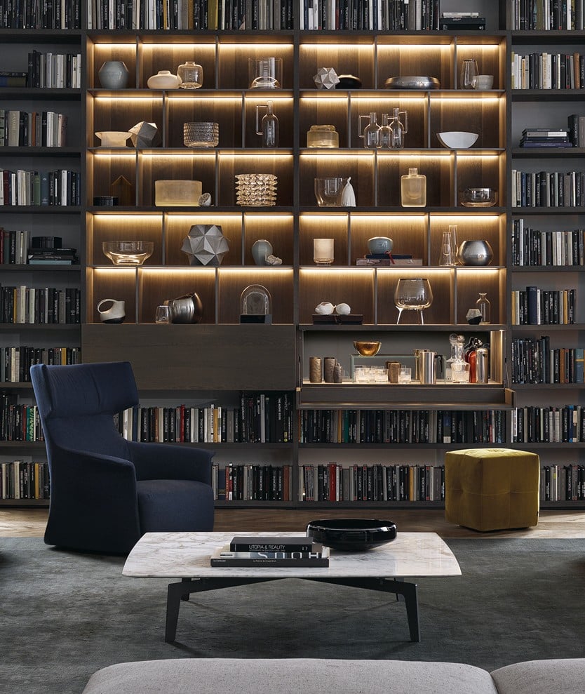 Wall System composition with spessart oak structure, matt slate lacquered grilles and LED light. Jet protruding flap in spessart oak and equipped compartment in bar version with white mirror back, Jet flap door interior covered in 02 nero leather and extra-clear transparent glass bridge shelf. Onda pouf in removable Persia 1403 ocra velvet. Tribeca coffee table with matt brown nickel structure and glossy calacatta oro marble top.